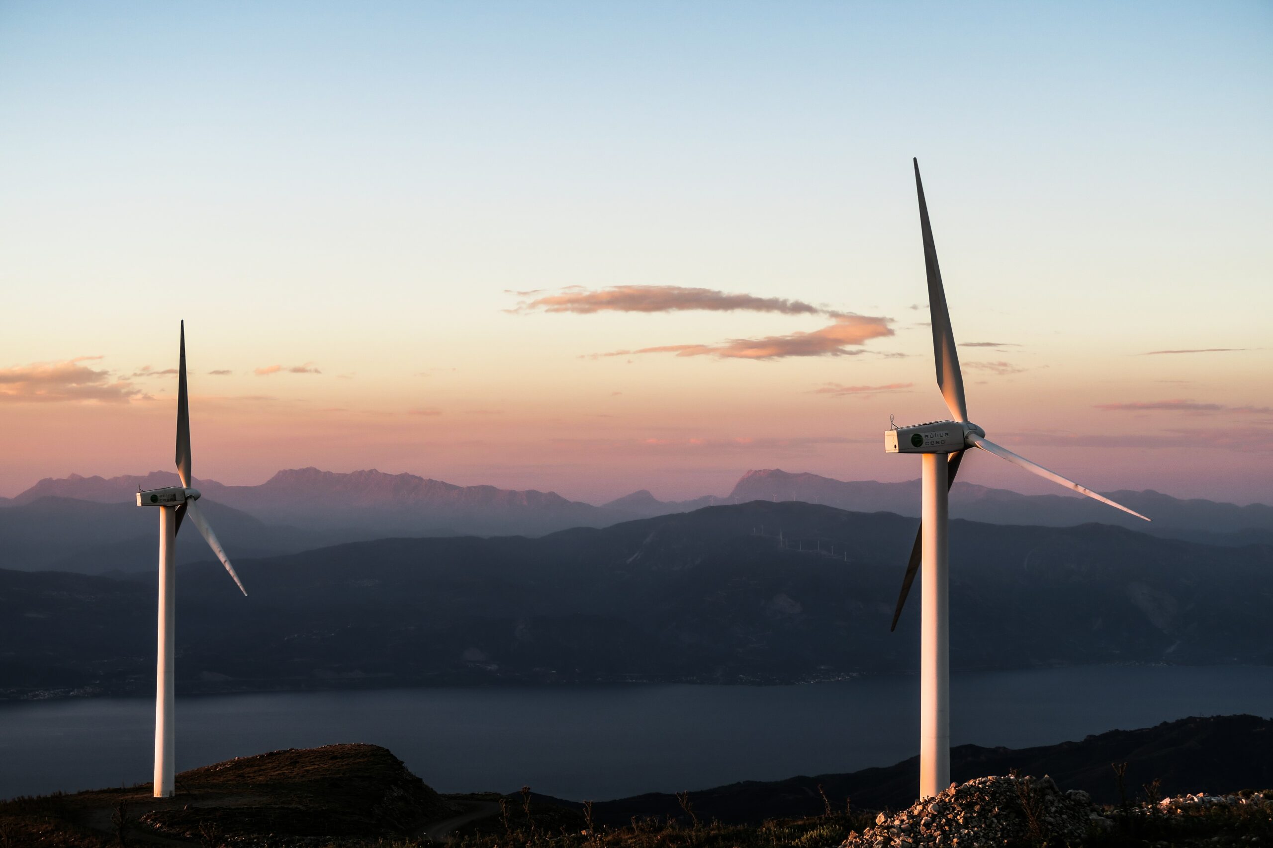 This image depicts two wind turbines situated on top of a mountain. The turbines are likely generating renewable energy from the wind that blows across the mountain. The image aligns with our company's shared goal of enabling a better future for all by promoting the use of clean energy sources that reduce our dependence on fossil fuels and mitigate the harmful effects of climate change. Wind turbines are one of many technologies that can help us transition to a more sustainable and environmentally-friendly energy system.