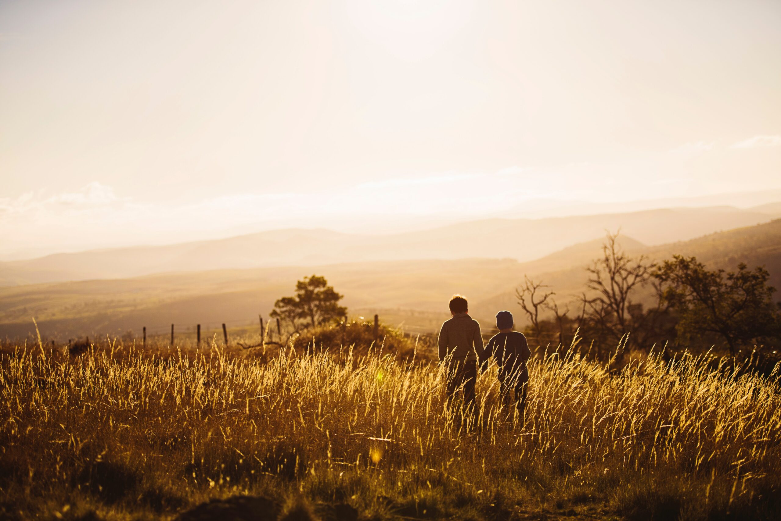 Two children walk in a field at sunset. The image symbolises the importance of human connection and the need to preserve natural spaces to ensure that they remain accessible to all for generations to come. It also represents the importance of promoting sustainable practices that enable us to enjoy nature without causing harm to the environment.