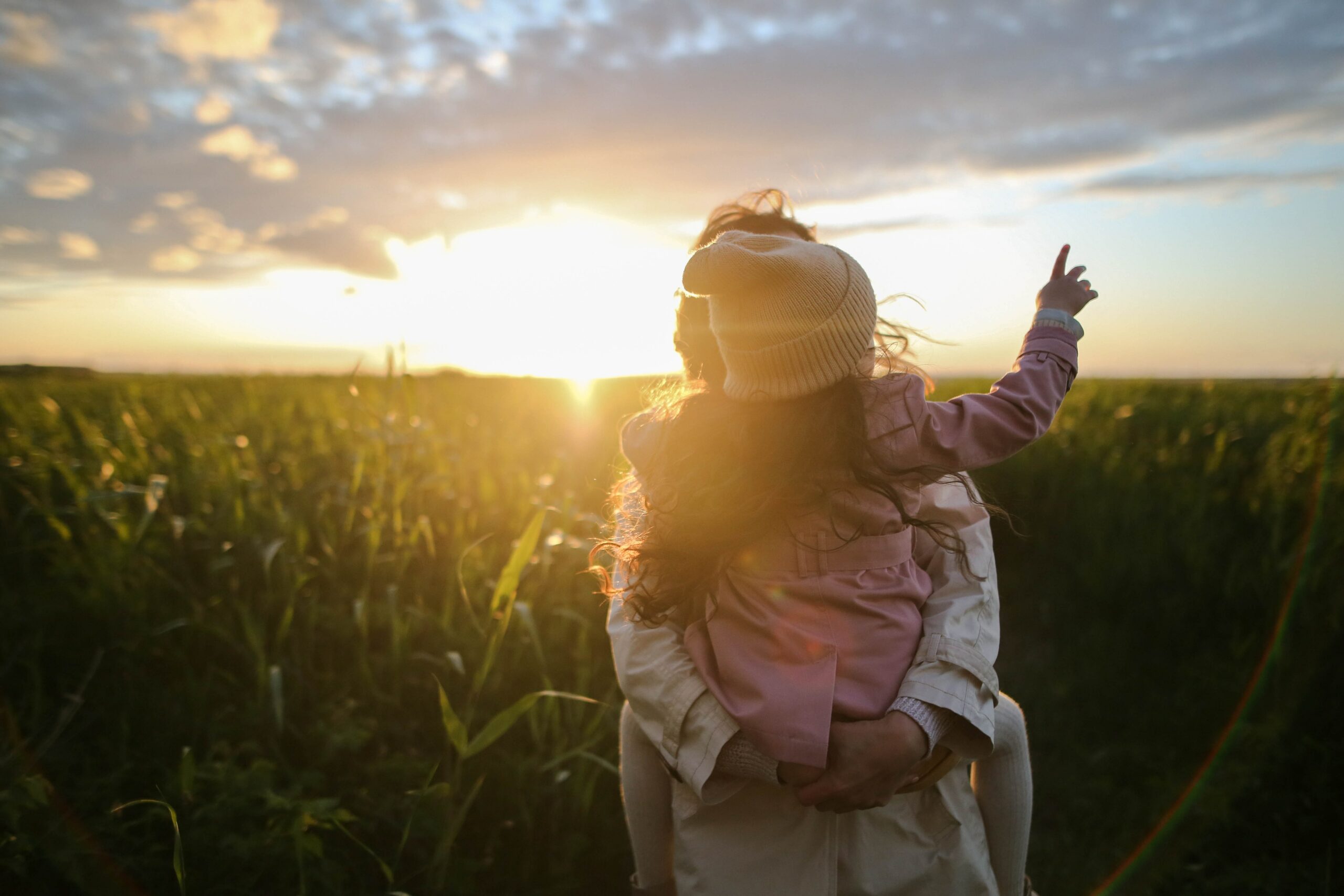 The image you described depicts a mother carrying her child in a field at sunset. The image symbolises a mother's love and care for her child and the beauty of nature during sunset. This image could represent a sustainable future where all individuals are treated with love and care and where nature is valued and protected. It can serve as a reminder of the importance of nurturing human relationships and preserving our environment for the well-being of future generations.